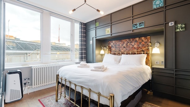 A modern hotel room with a large bed, a radiator, a heater, and a view of the cityscape. - GuestReady - Charming Covent Garden Retreat (London)