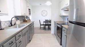 A modern kitchen with white cabinets, a stainless steel refrigerator, and a dining area with a clock on the wall. - Secluded Modern Farmhouse on 3 Acres - 4m. from all things Chickasha (Ninnekah)