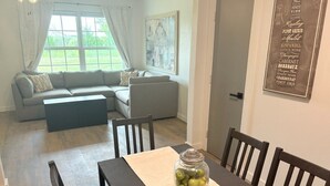 A modern living room with a gray sofa, a coffee table, and a dining area with a table and chairs. There is a jar of lemons on the table. - Secluded Modern Farmhouse on 3 Acres - 4m. from all things Chickasha (Ninnekah)