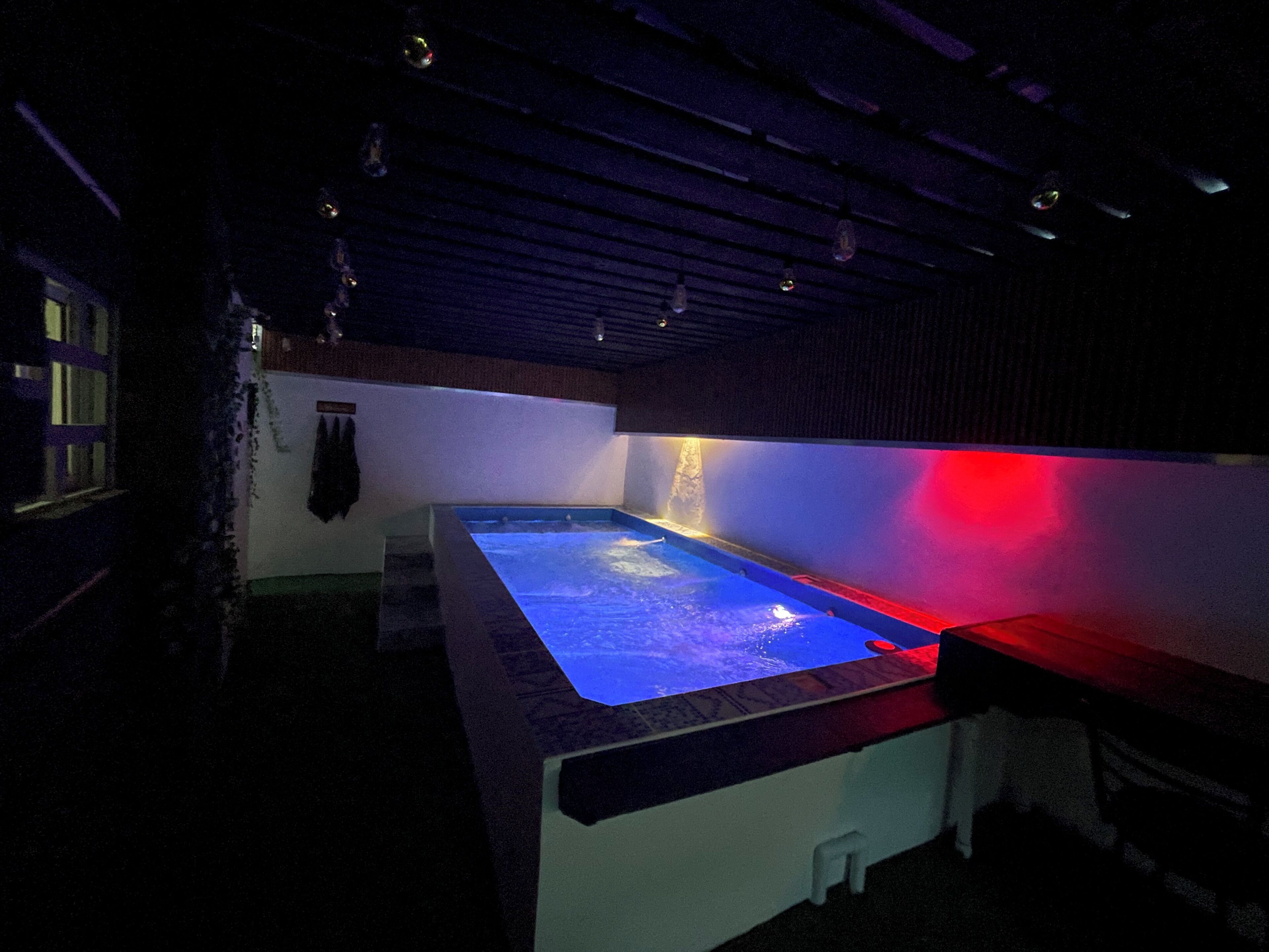 A dimly lit room with a large rectangular pool, a small waterfall feature, and a red light on the right side.