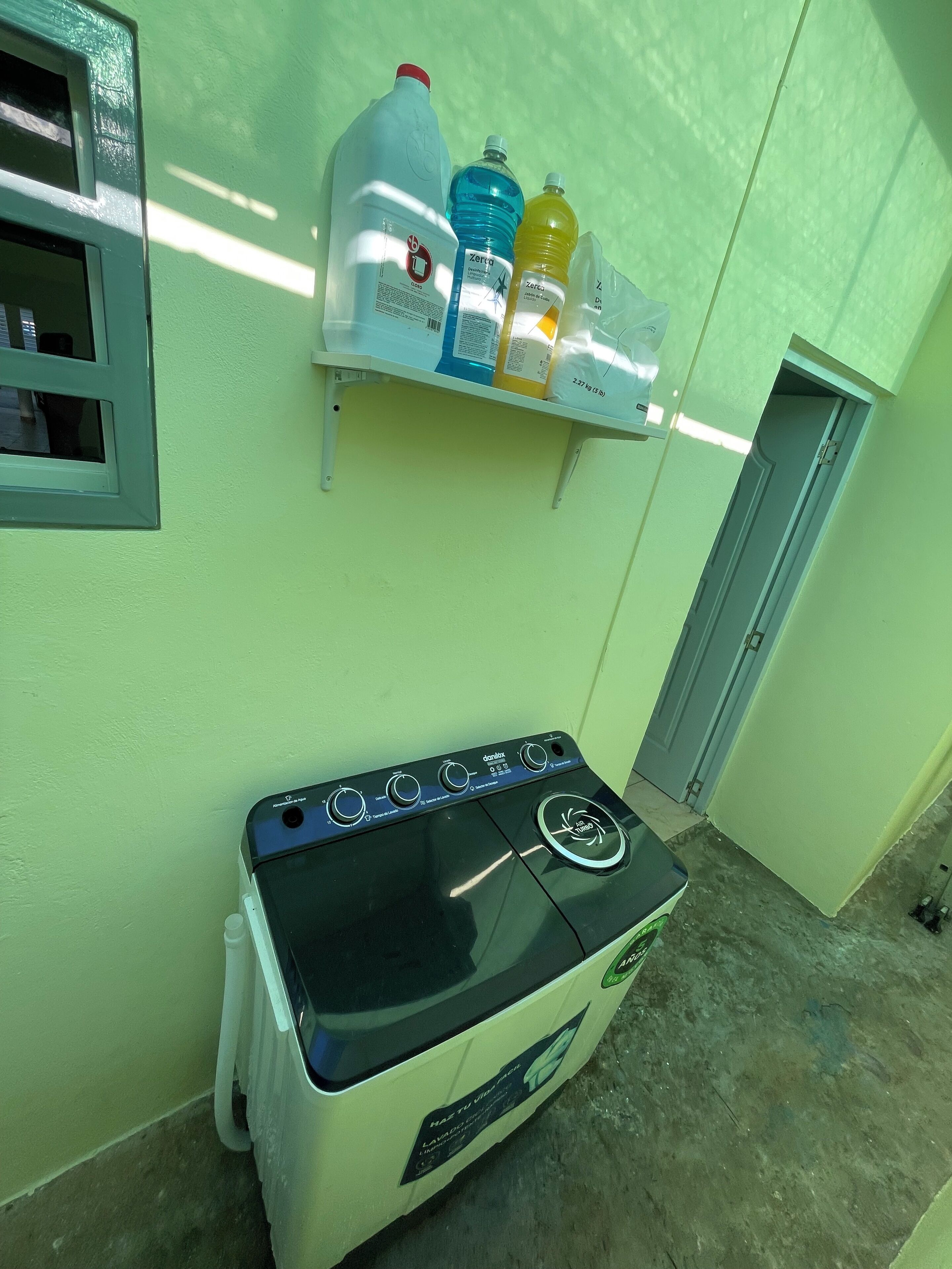 A compact kitchen with a gas stove, a small shelf holding water bottles, and a window with a view.