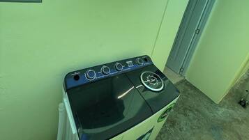 A compact kitchen with a gas stove, a small shelf holding water bottles, and a window with a view.