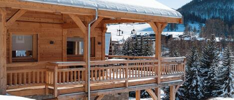 Una cabaña de madera con balcón, rodeada de árboles nevados y montañas.