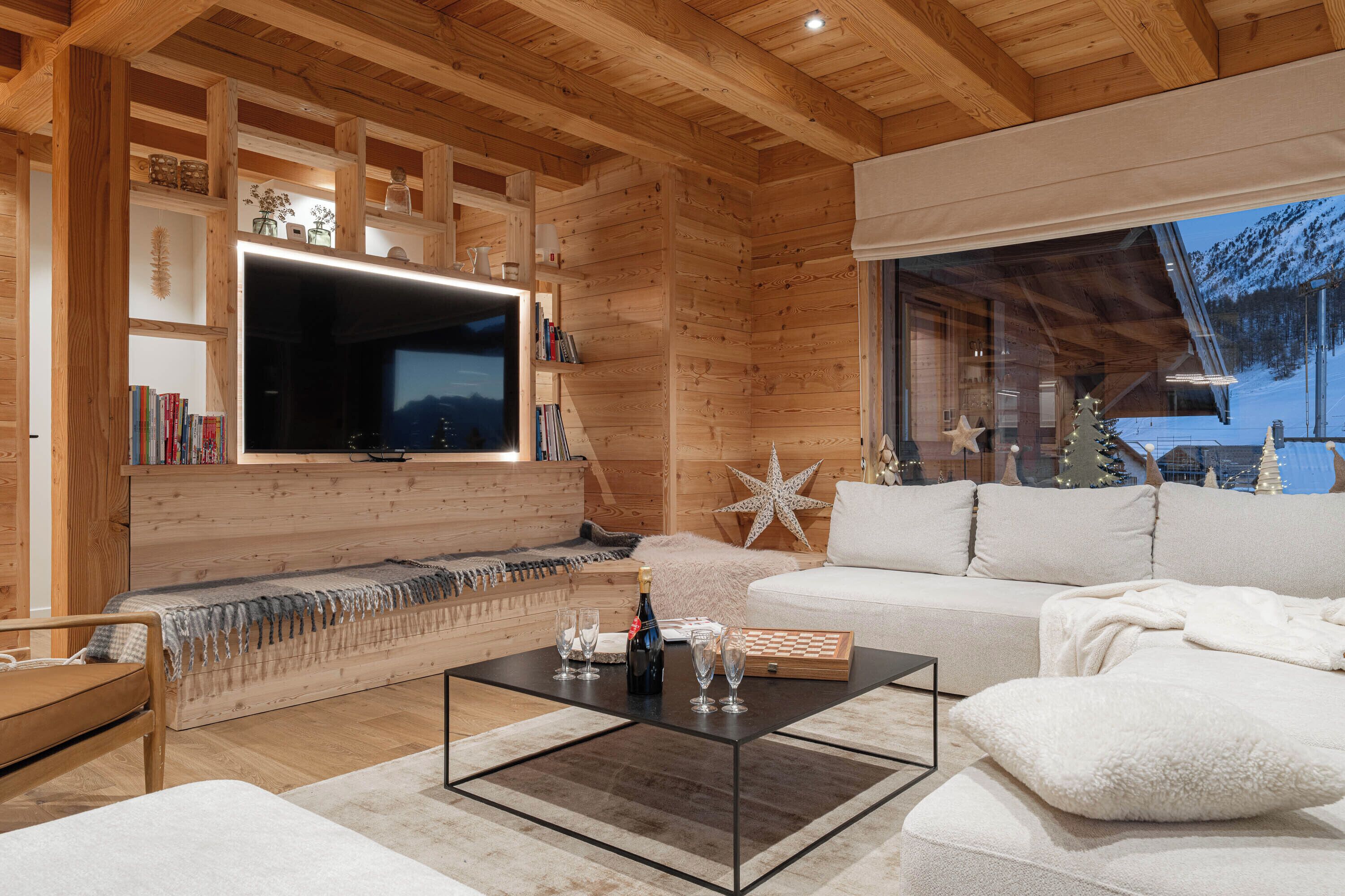 Una sala de estar acogedora con detalles de madera, un televisor de pantalla plana grande, un sofá, una mesa de centro y una estantería.