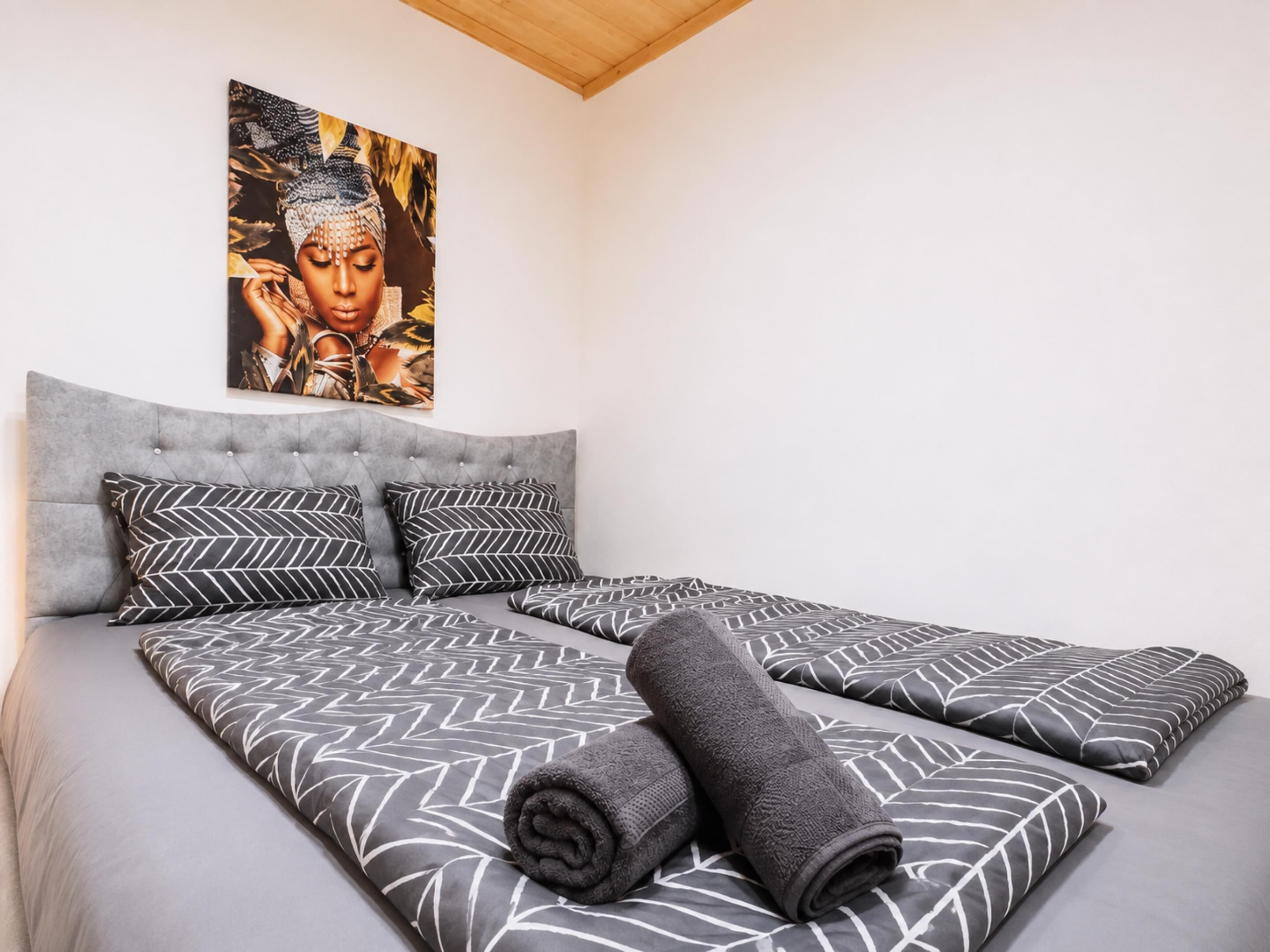 A bedroom with a large bed, grey upholstered headboard, patterned bedding, and a wall-mounted artwork.