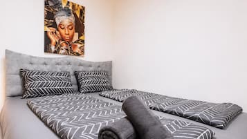 A bedroom with a large bed, grey upholstered headboard, patterned bedding, and a wall-mounted artwork.