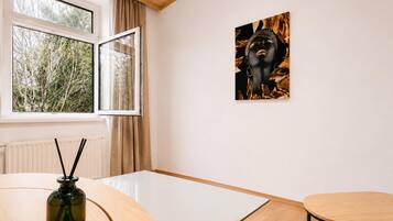 A room with a table, a chair, a window with curtains, and a wall-mounted artwork.
