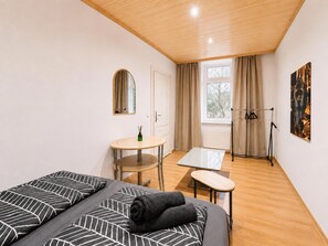 Een compacte hotelkamer met twee bedden, een kleine tafel, een spiegel, een raam met gordijnen en een radiator.
