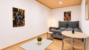 A modern room with a grey sofa, a round table, and two wall-mounted paintings.