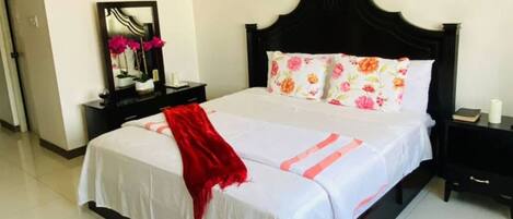 A neatly made bed with a white bedspread and red throw, a black headboard, and floral pillows.