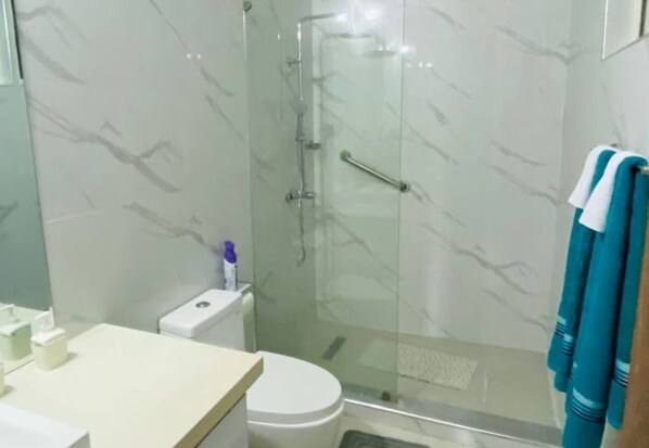 Un baño con cabina de ducha de vidrio, inodoro y lavabo con espejo.