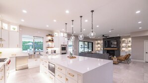 A modern kitchen with a large island, white cabinetry, and pendant lighting. - Luxury Outdoor Living - Heated Pool and Hot Tub (Chandler)