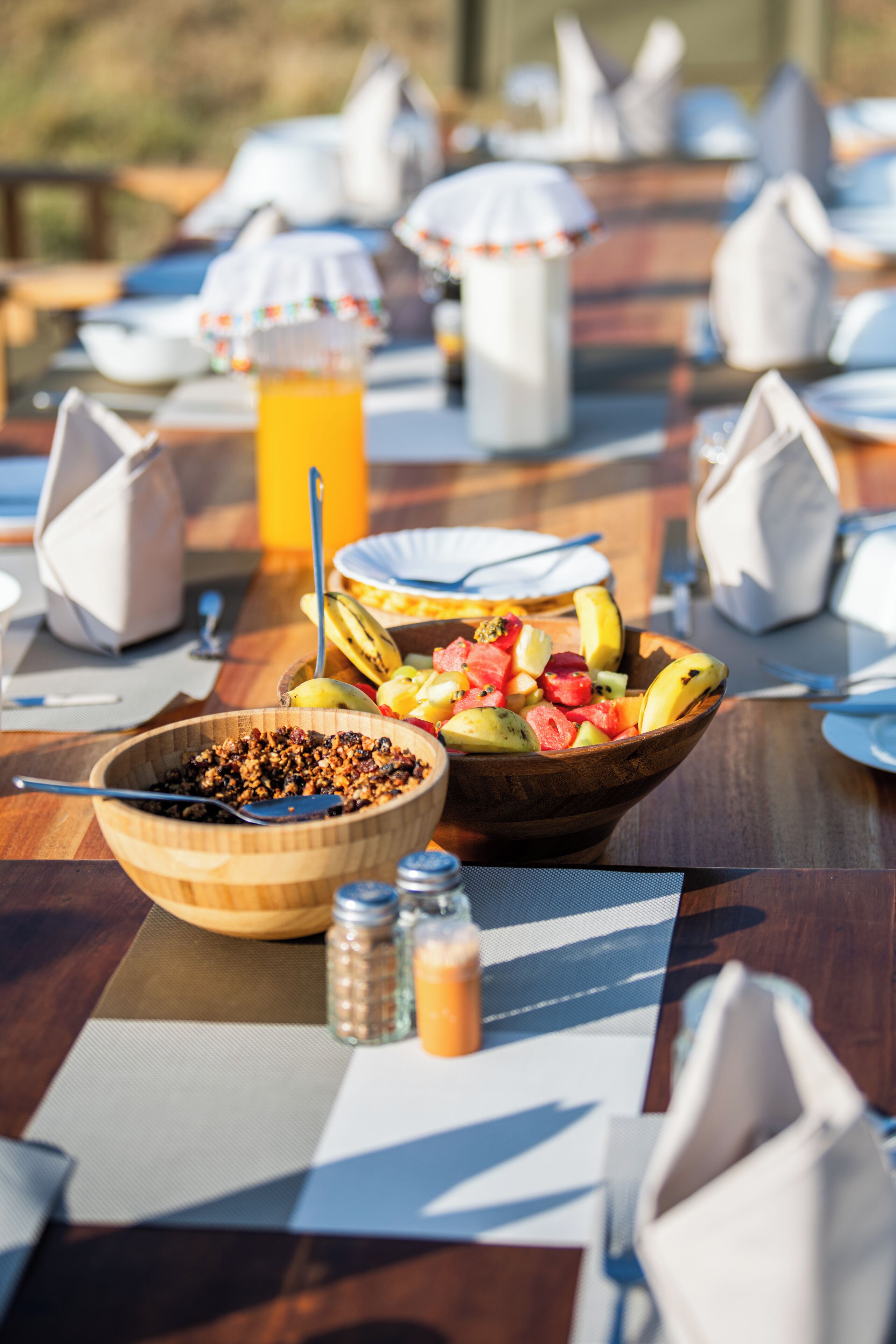 Et morgenbord med skål med cornflakes, en skål med frugt og et glas appelsinjuice.