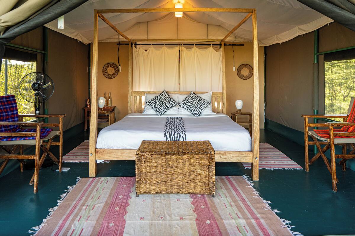 A four-poster bed with a canopy, a wicker bench, and two wooden chairs with cushions.