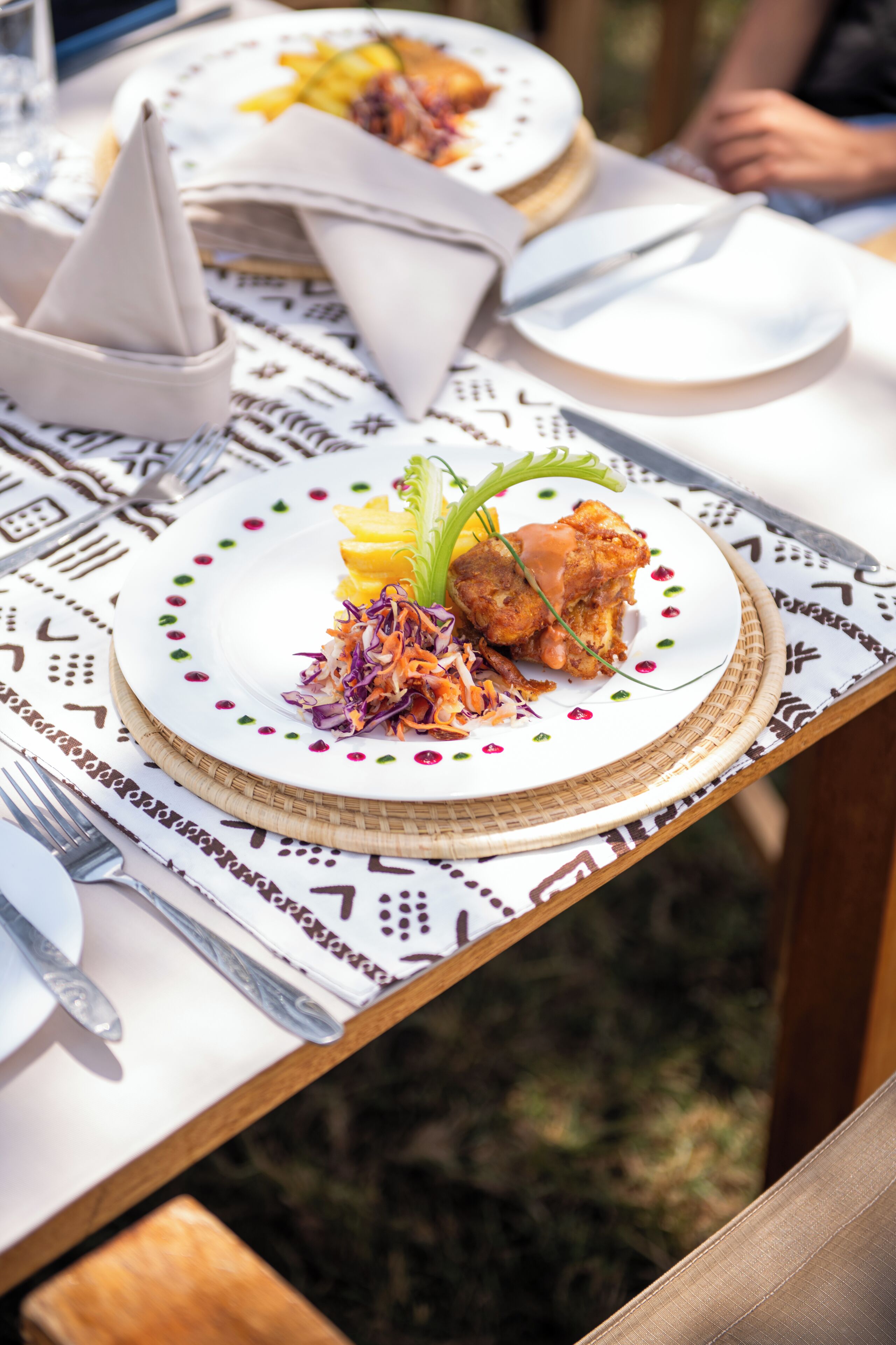 Una mesa de comedor con un plato de comida, utensilios y un cono para servilletas.