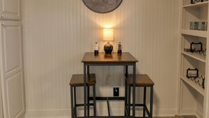 Um quarto com uma mesa de madeira e duas cadeiras, uma luminária na parede e uma prateleira com objetos decorativos.