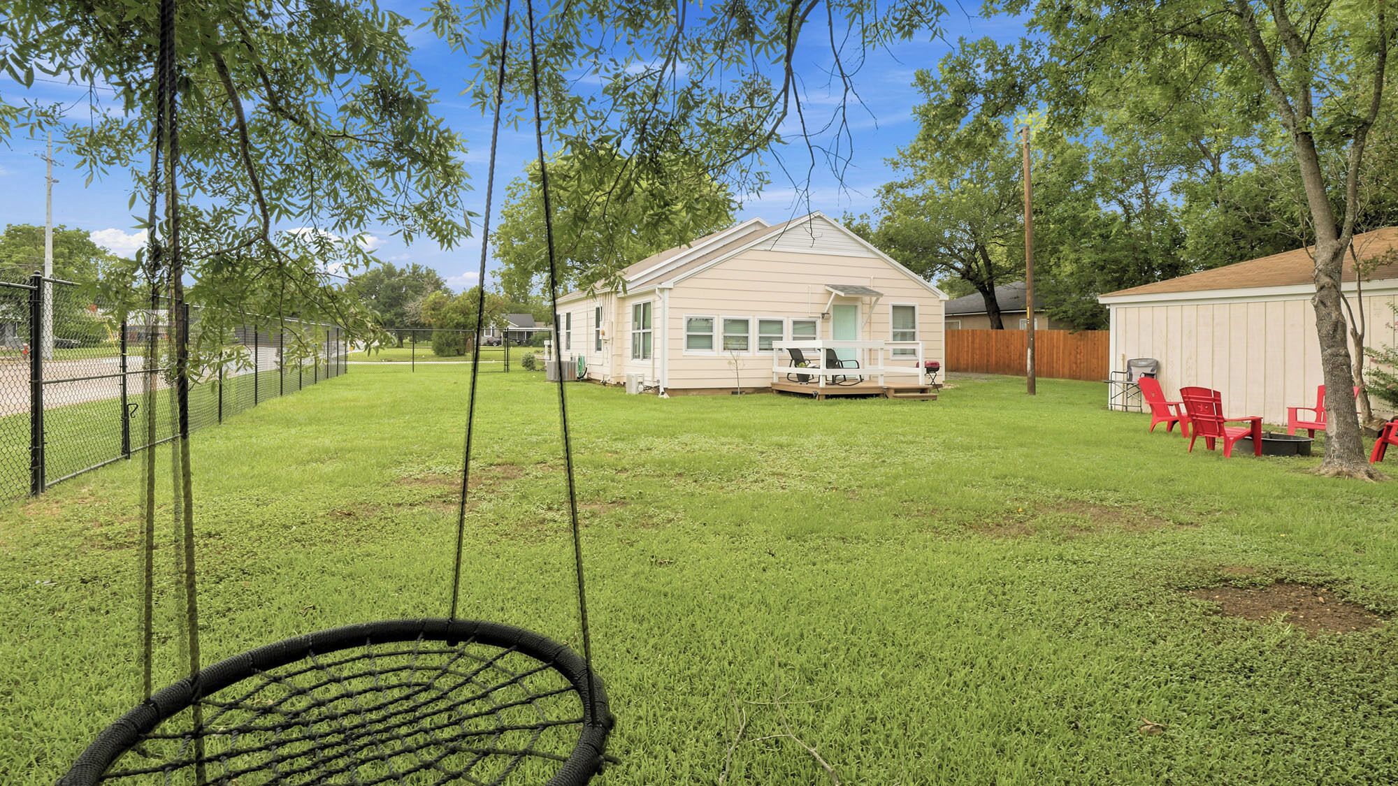 A backyard with a swing set, a house, and a fenced area.