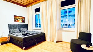 Une chambre à coucher comprenant un lit, une chaise, une table de chevet et une fenêtre avec des rideaux.