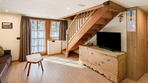 Quarto com escada de madeira, televisão em uma cômoda, um sofá e janela com cortinas.