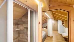 Interior de madeira com chuveiro, cama e um banco.