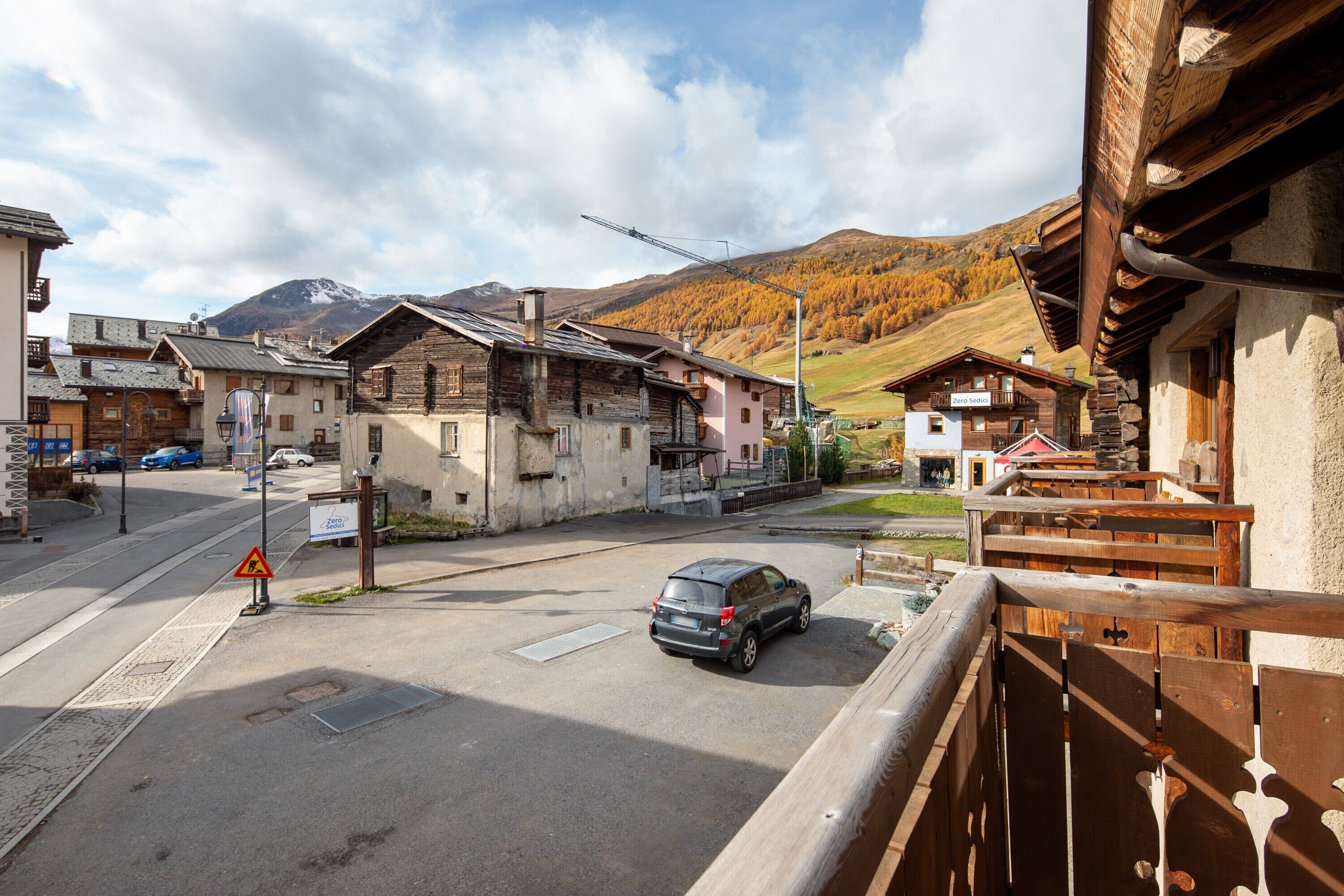 A mountain village with traditional wooden houses, a street with a car, and a mountain in the background.