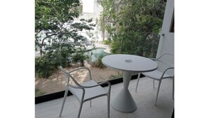 A balcony with a round table and two white chairs, overlooking a garden and a pool. - Practical and Comfortable Loft (Tulum)