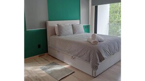A neatly made bed with striped bedding, a grey headboard, and a window with a view of greenery. - Practical and Comfortable Loft (Tulum)