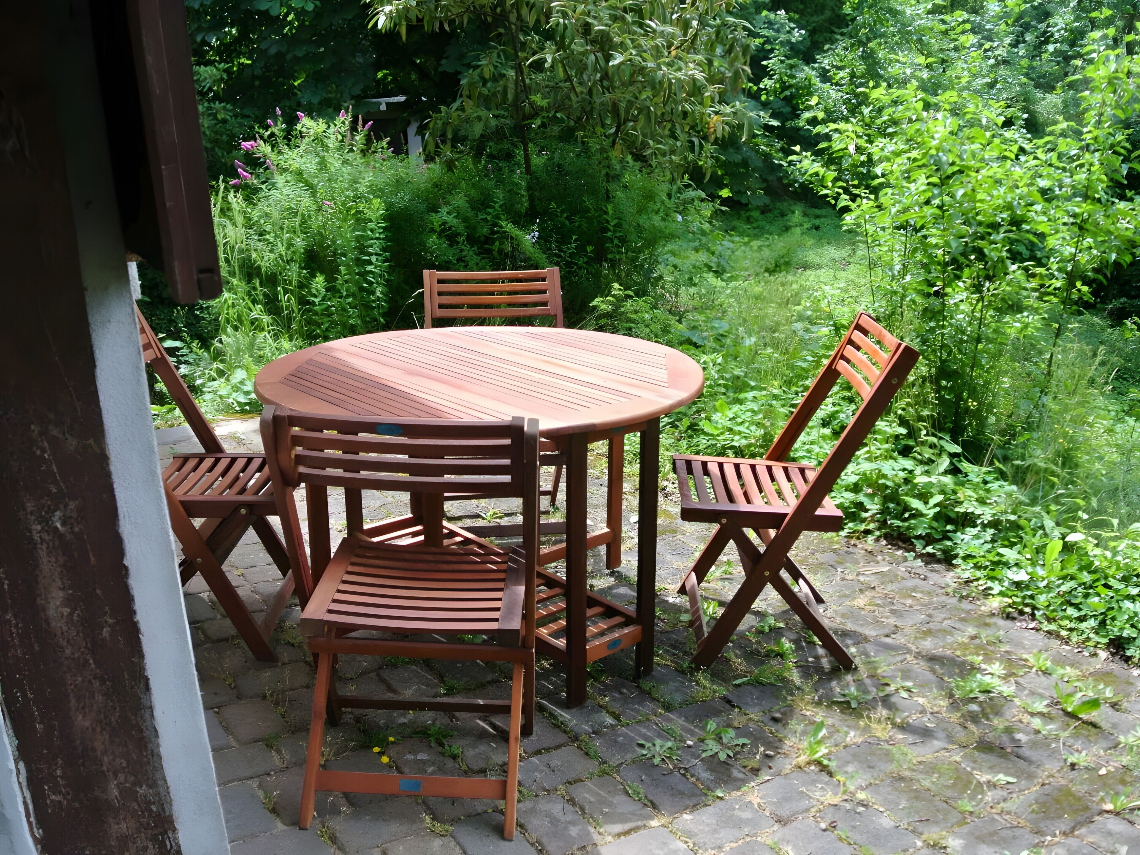 A round wooden table with four chairs in a garden setting.