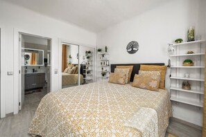 Un dormitorio con cama, armario, espejo y estantes con objetos decorativos.