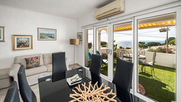 A modern living room with a sofa, a dining table with chairs, and a large window with a view of the outdoors. - Apartment 'Gudrun' with Sea View, Wi-Fi and Air Conditioning (Praia do Carvoeiro)