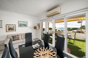 A modern living room with a sofa, a dining table with chairs, and a large window with a view of the outdoors. - Apartment 'Gudrun' with Sea View, Wi-Fi and Air Conditioning (Praia do Carvoeiro)