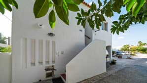 A white building with a staircase, a security camera, and a small outdoor area with a car and plants. - Apartment 'Gudrun' with Sea View, Wi-Fi and Air Conditioning (Praia do Carvoeiro)