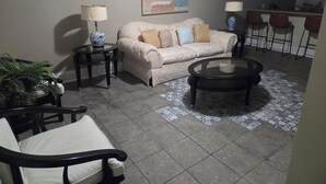 Un salon avec un canapé beige, deux tables d’appoint avec des lampes, une table basse et un tapis à motifs.