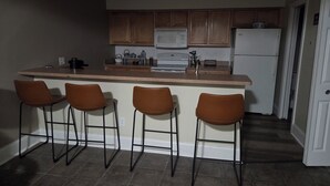 Une cuisine dotée d’un îlot central, de quatre tabourets de bar, de meubles en bois, d’un four à micro-ondes, d’une cuisinière et d’un réfrigérateur.
