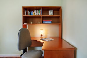 Un bureau en bois avec une chaise, une bibliothèque remplie de livres, une horloge et une lampe.