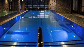 A large indoor swimming pool with a stone wall backdrop and a seating area with chairs. - Skistar Lodge Hundfjället  (Lima)