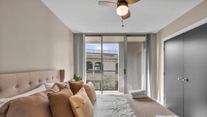 Una camera da letto con un letto grande, una ventola a soffitto, una porta scorrevole in vetro che dà su un balcone e un armadio.