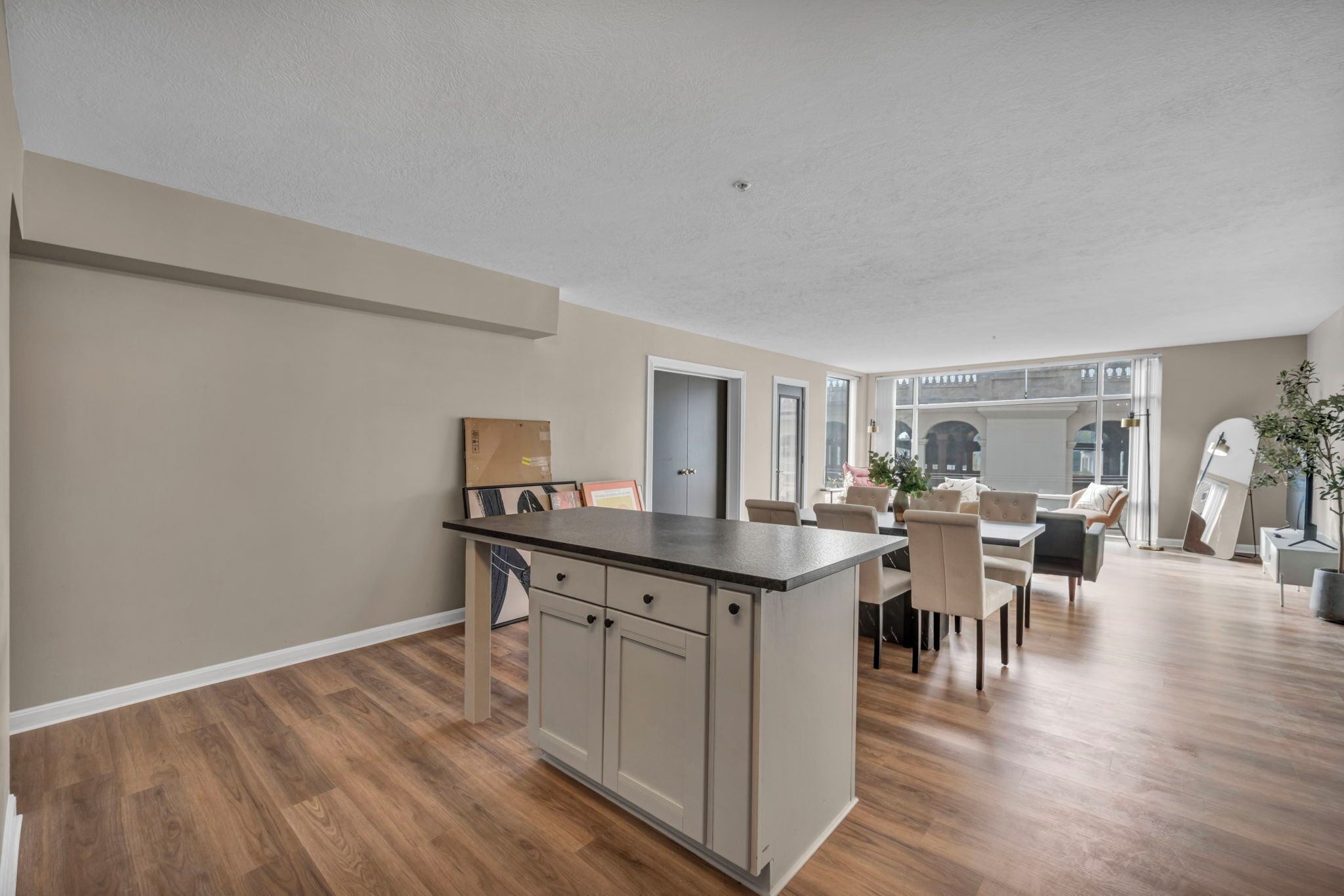 A spacious living area with a kitchen island, wooden flooring, and a dining area with chairs and a table.