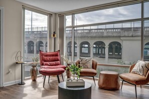 A spacious room with large windows, a red chair, a brown armchair, and a round coffee table. - Charming 2-bedroom apartment, City-Life, Free Parking, 24/7 Hour Gym (Cleveland)