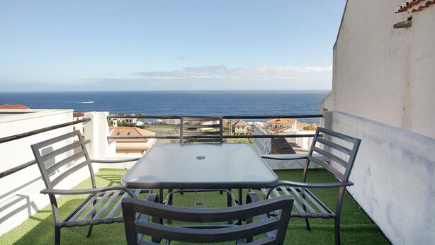 A balcony with a table and chairs, overlooking a coastal view.