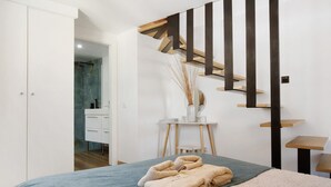 A bedroom with a bed, a desk, a chair, a staircase, and a bathroom.