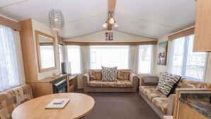A cozy living area with a round wooden table, two sofas, a television, and a kitchen area with a countertop and cabinets. - Hideaway Lodge (Abergele)