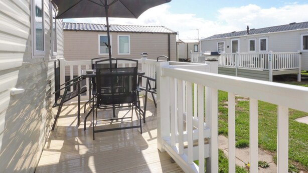 A deck with a table and chairs, a patio umbrella, and a white railing. - Hideaway Lodge (Abergele)