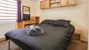 A bedroom with a bed, a desk, a television, and wooden cabinets. - Hideaway Lodge (Abergele)