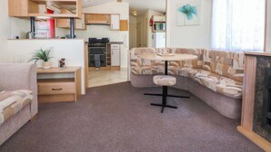 A compact living space with a kitchenette, a sofa, a small table, and a window. - Hideaway Lodge (Abergele)
