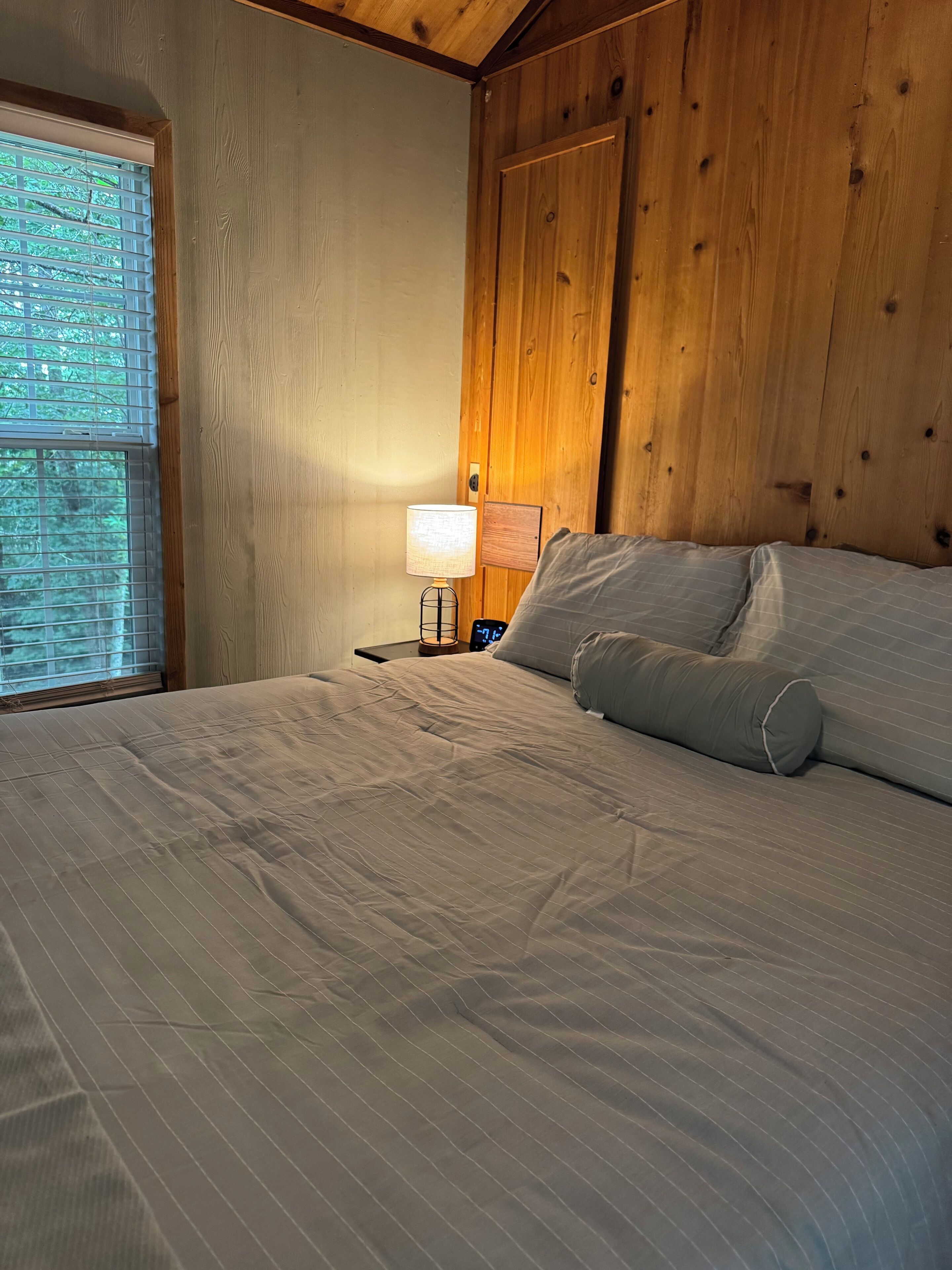 A bedroom with a bed, a nightstand, a lamp, and a window with blinds.
