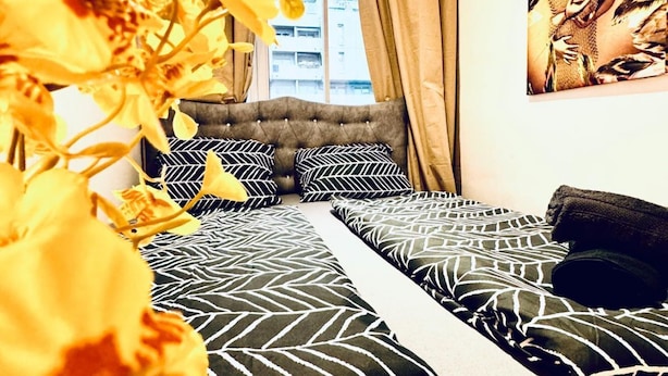 Une chambre à coucher avec une tête de lit capitonnée, une literie à motifs et une grande fenêtre avec des rideaux.