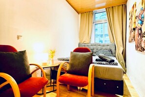 Une petite pièce agréable et confortable, avec un lit, deux chaises, une table et une fenêtre avec des rideaux.