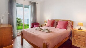 A bedroom with a bed, bedside tables, a chair, a dresser, and a view through a glass door. - Holiday Home 'Blissful Haven - Soulful Stays' with Sea View, Private Terrace and Wi-Fi (Porto Moniz)