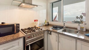 A kitchen with a gas stove, oven, microwave, and a large window with a view of the sea. - Holiday Home 'Blissful Haven - Soulful Stays' with Sea View, Private Terrace and Wi-Fi (Porto Moniz)